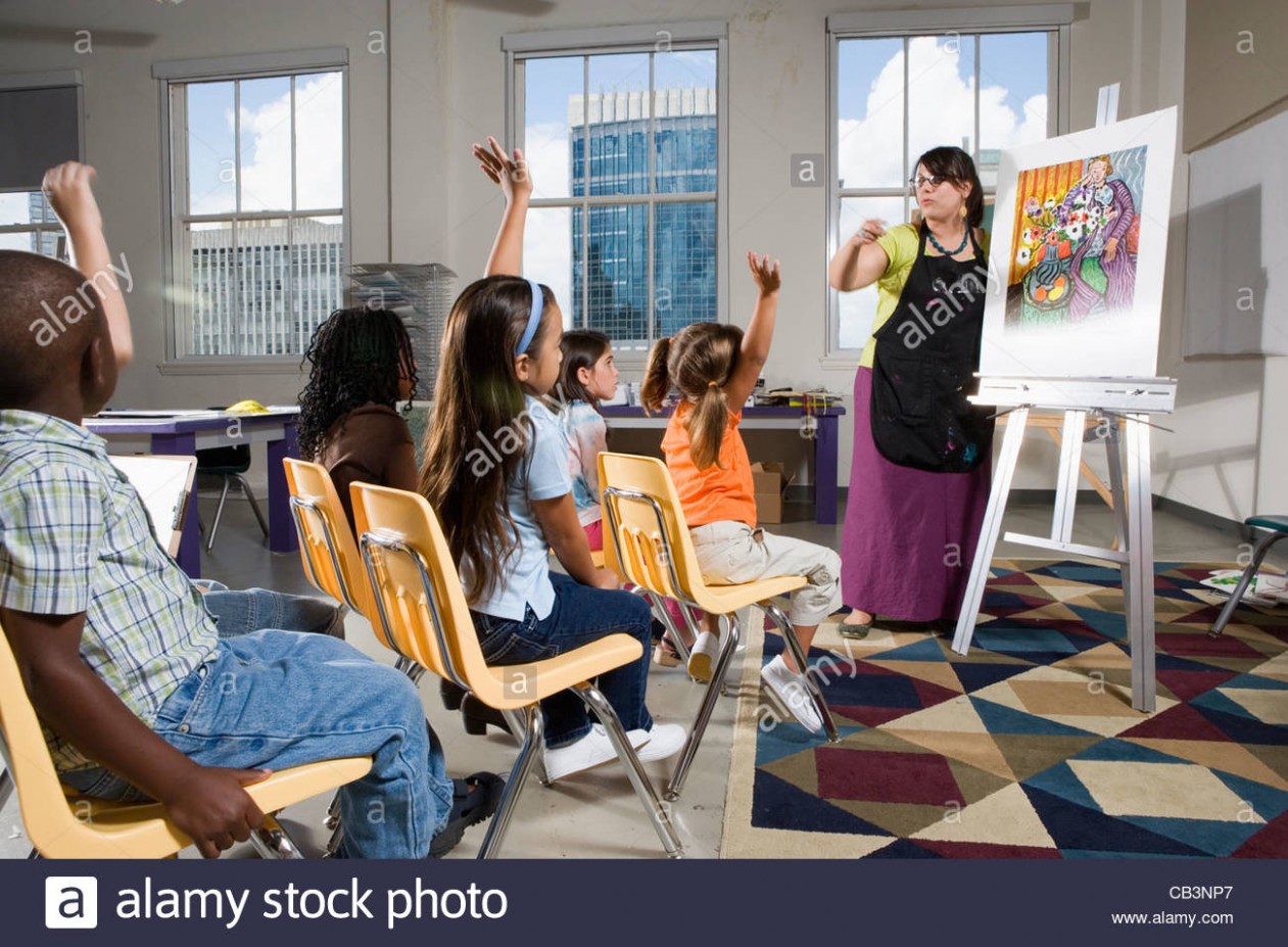 An Art Teacher Standing By Easel Teaching Her Young Students In ..